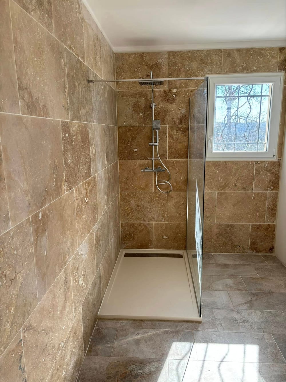Douche à l'italienne en travertin avec paroi de verre